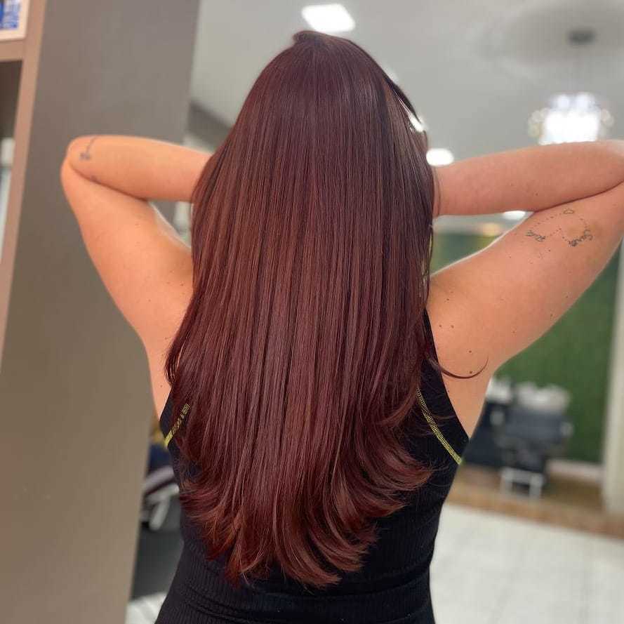 Mulher de costas no salão com blusa preta e cabelo em tom de castanho com fundo rosado
