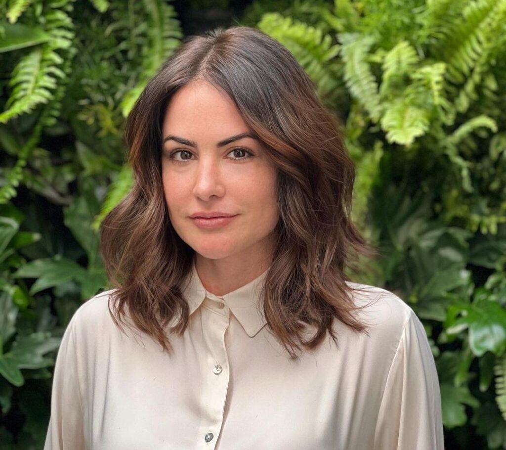 Mulher de camisa bege no salão com cabelo long bob em tons de castanho amendoado