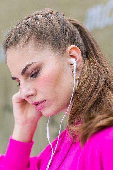 Mulher com cabelos loiros presos em um rabo de cavalo ouve música com fones de ouvido