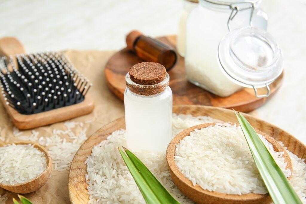 imagem de água de arroz num vidro com rolha junto com escova de cabelo e grãos de arroz