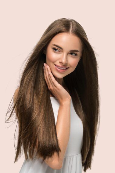 Mulher de cabelo longo castanho e liso com alisamento a laser no fundo rosta segurando o queixo com a mão