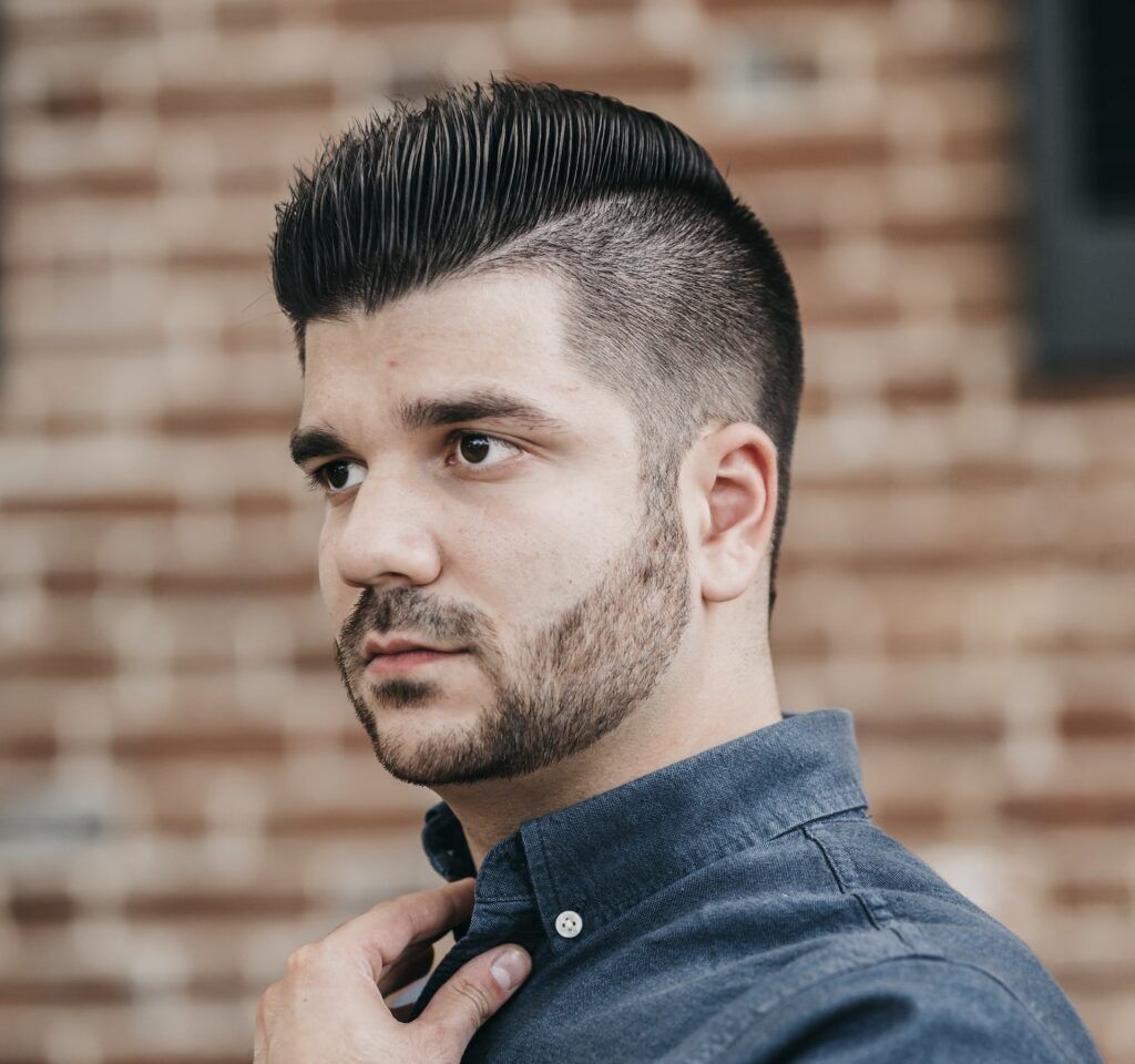 Homem posa segurando a gola da camisa com corte undercut no cabelo grosso preto e liso com gel