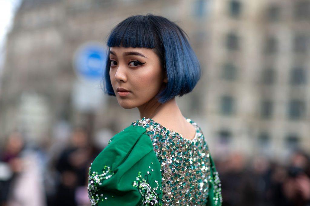 Mulher com traços orientais de cabelo curto, franja e cor azul olha para trás em direção à câmera