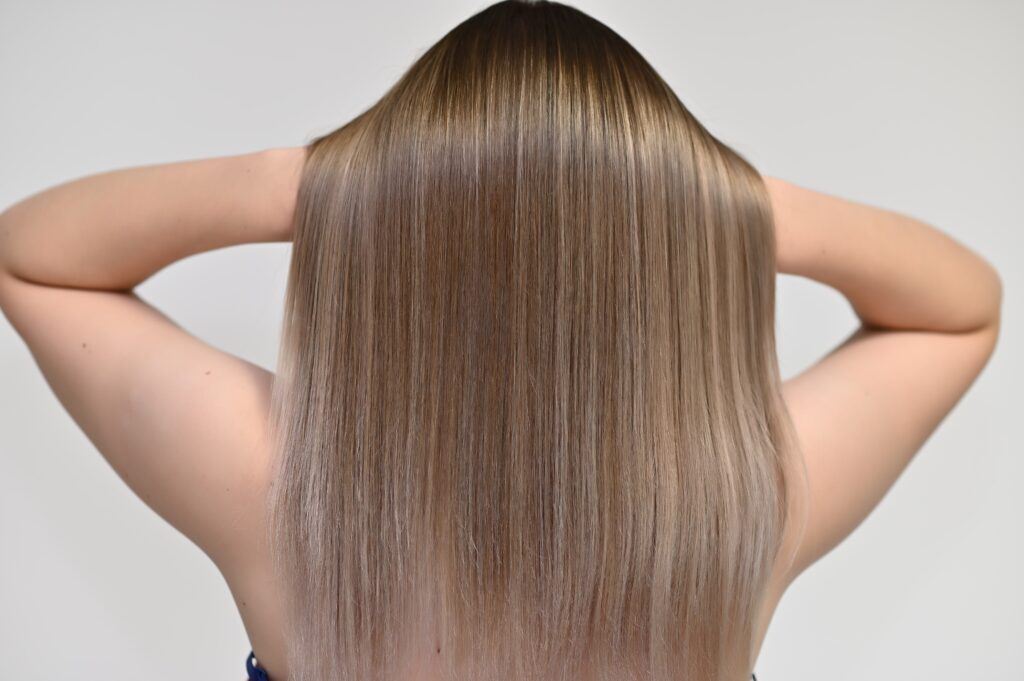 Mulher de costas segurando o cabelo liso e loiro com progressiva sem formol com as mãos