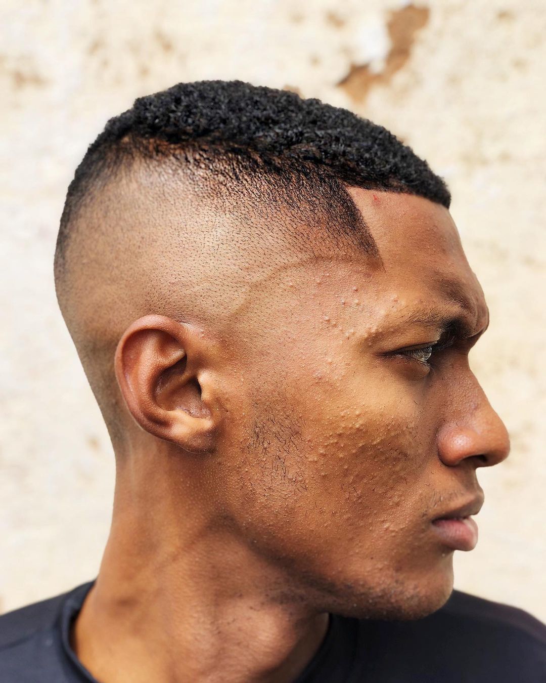 Homem de perfil ao ar livre com corte high fade navalhado no cabelo