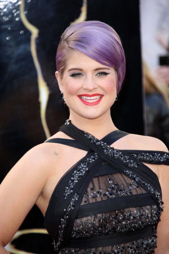 Kelly Osbourne posa em evento com vestido preto e cabelo roxo curto liso no rosto triangular