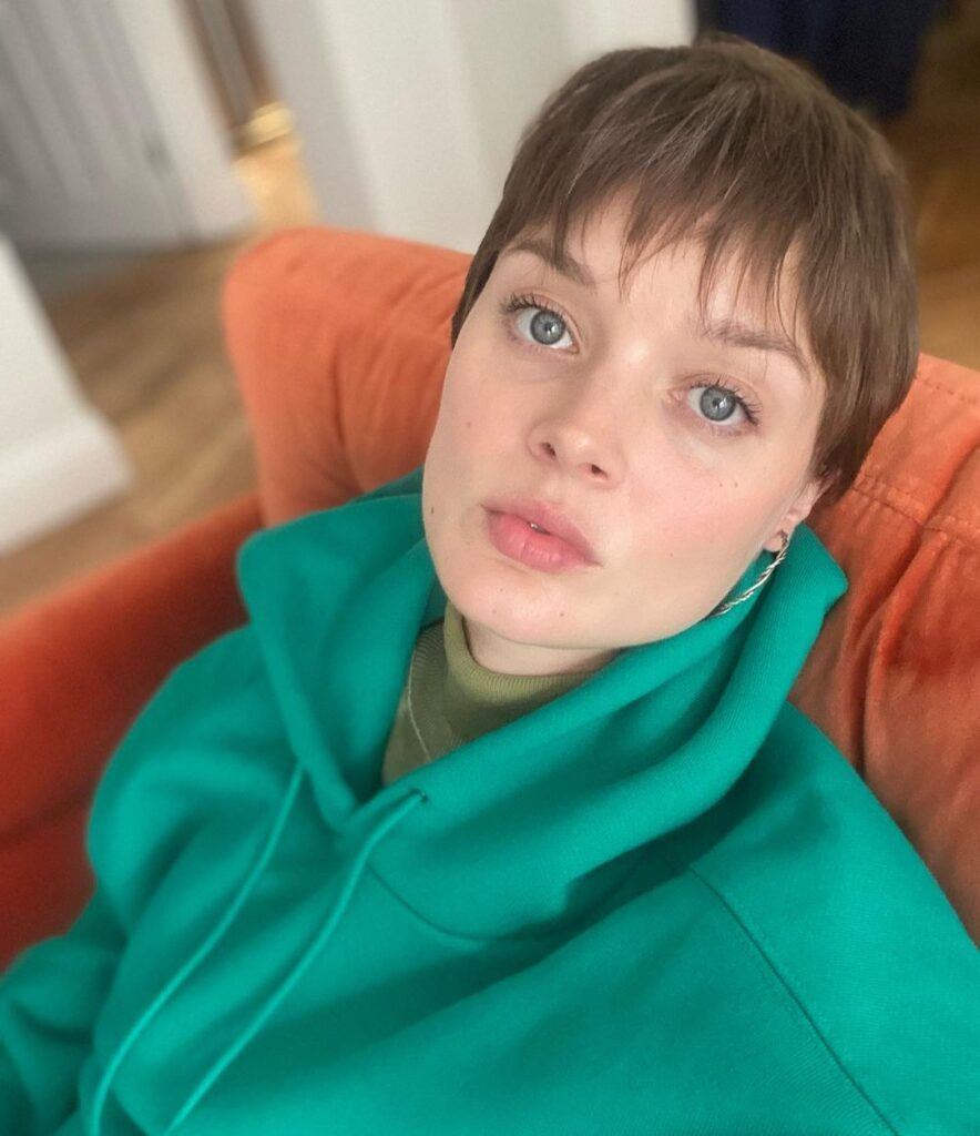 Atriz Bella Heathcote posa com moletom verde e cabelo curto pixie com franja no rosto triangular
