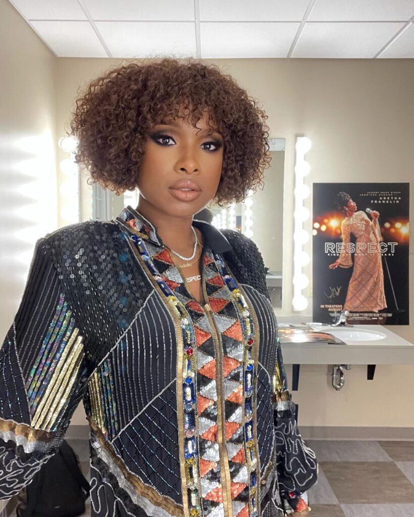 Atriz e cantora Jennifer Hudson posa com jaqueta brilhante e cabelo short bob com franja cacheada no rosto triangular