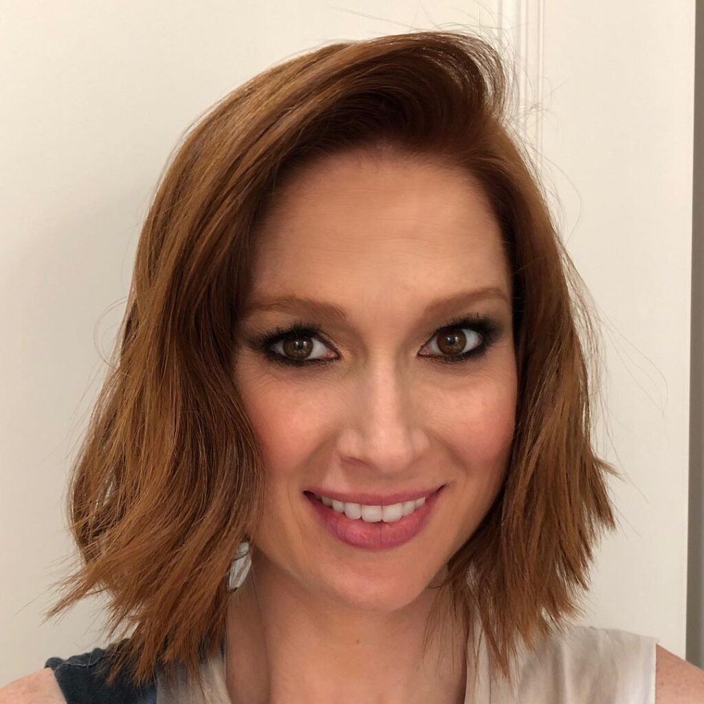 Atriz Ellie Kamper posa com vestido preto e branco e cabelo ruivo curto chanel de bico no rosto triangular