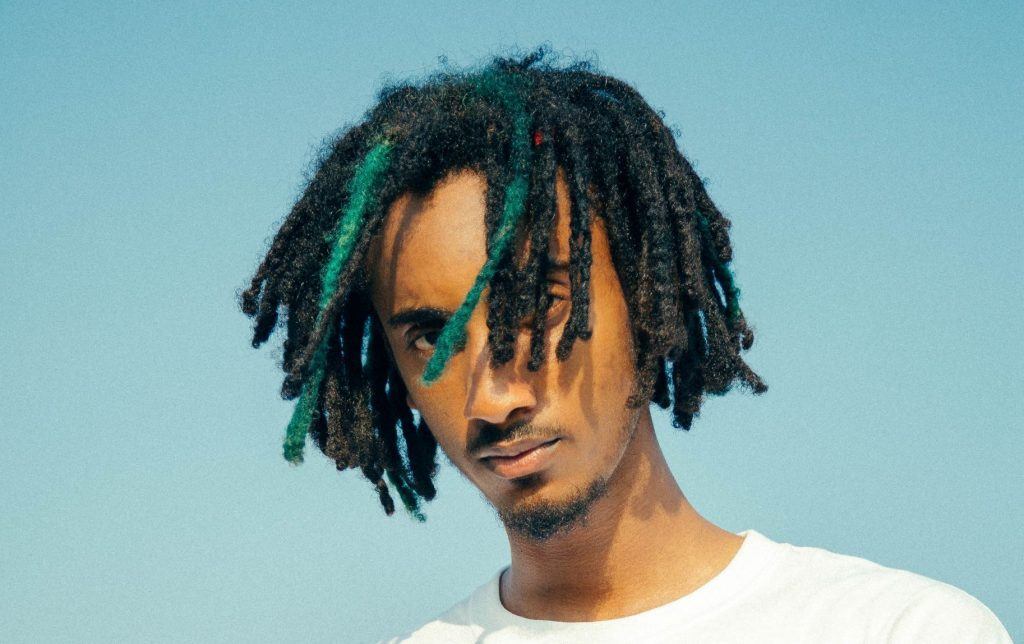 Homem de cabelos crespos com dreadlocks curtos, ao ar livre, sob o céu azul