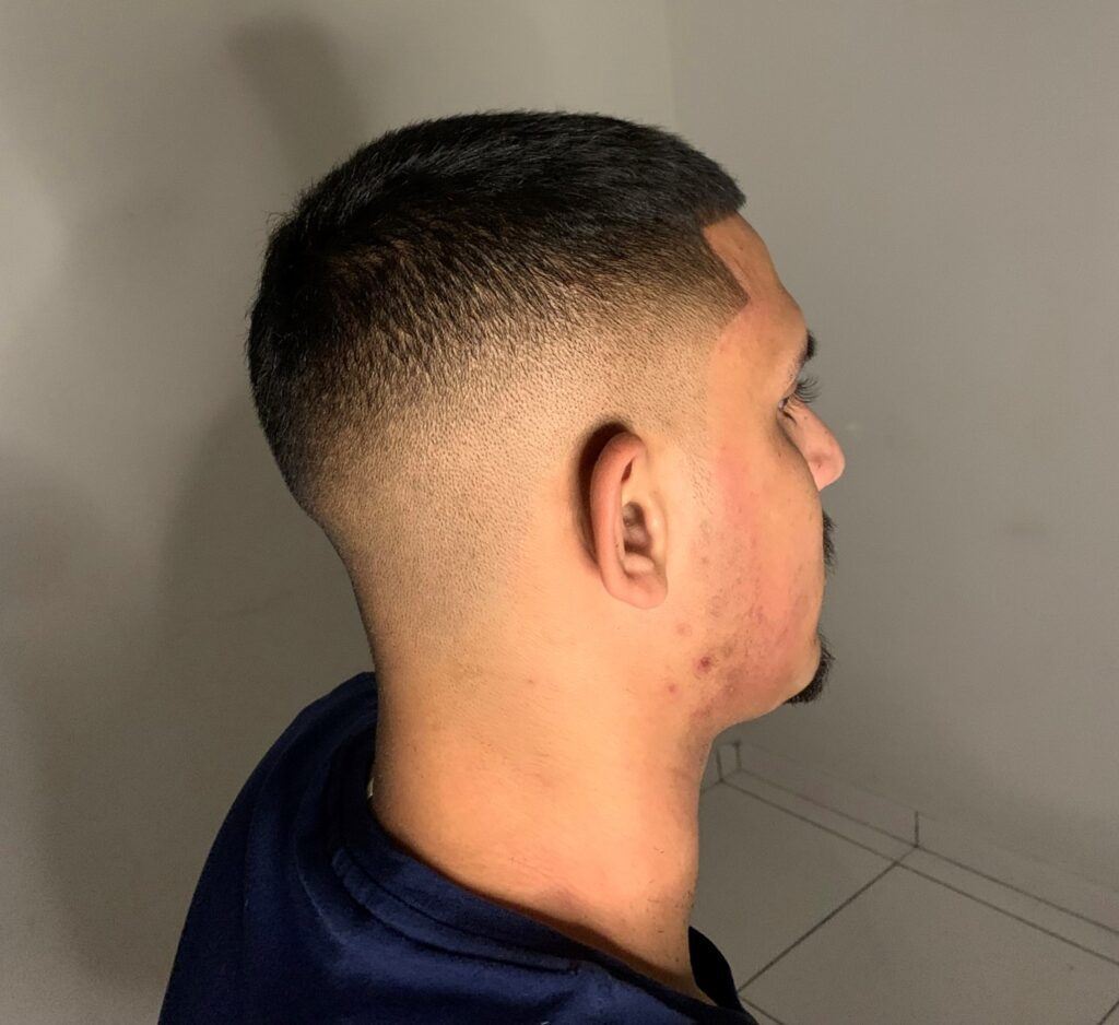 Homem com camiseta azul escura de perfil no salão com corte degrade estilo militar ou social no cabelo