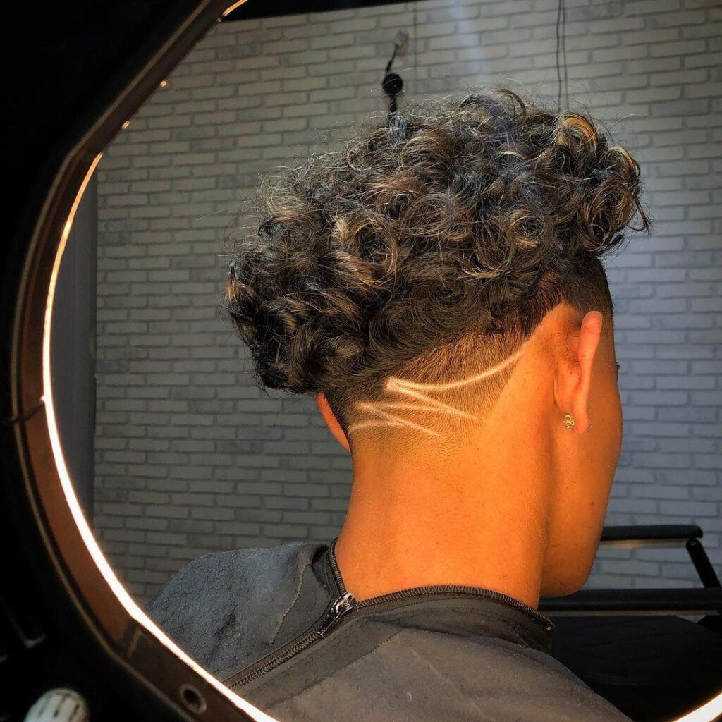 Homem de costas no salão com corte degradê no cabelo estilo taper fade cacheado com risco