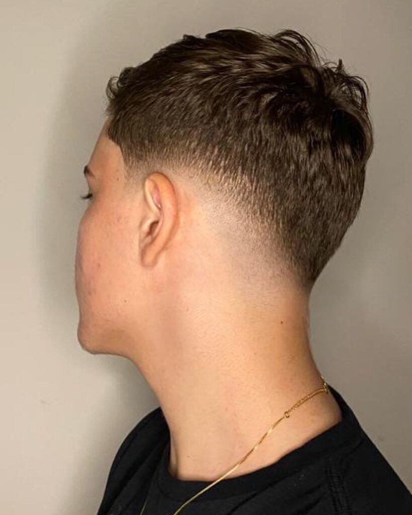 Homem de perfil no salão com corte degrade em v no cabelo estilo low fade