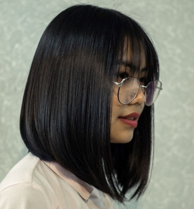 Mulher posa de perfil com cabelo chanel de bico com franja e óculos