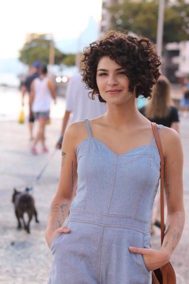 Influenciadora Gabi Vasconcellos com cabelo solto cacheado na altura do queixo e macacão de alças