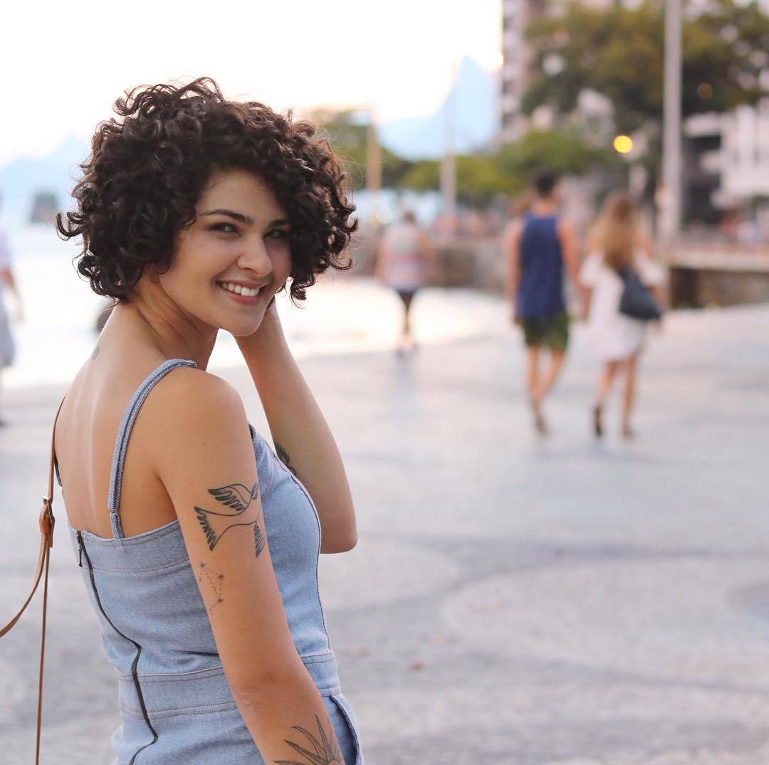 Influenciadora Gabi Vasconcellos com cabelo solto cacheado na altura do queixo e macacão de alças