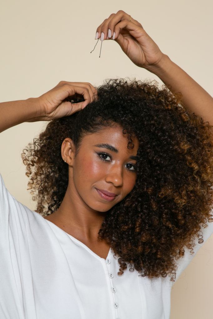 Modelo prende os cabelo com grampos para fazer o preso na lateral com o cabelo solto