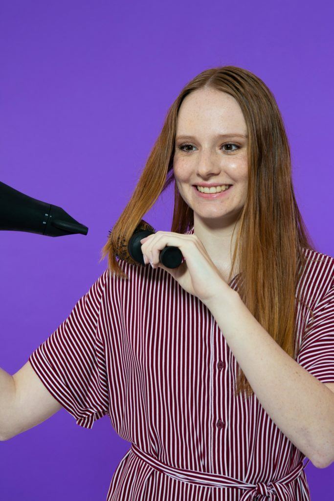 modelo secando o cabelo com secador e escova.