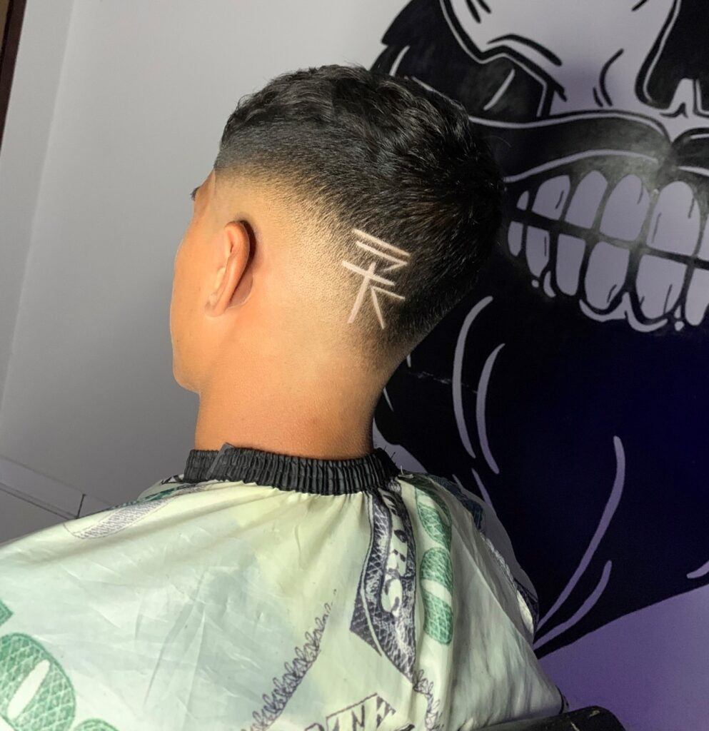 Homem de costas no salão e corte degrade em v com desenho no cabelo