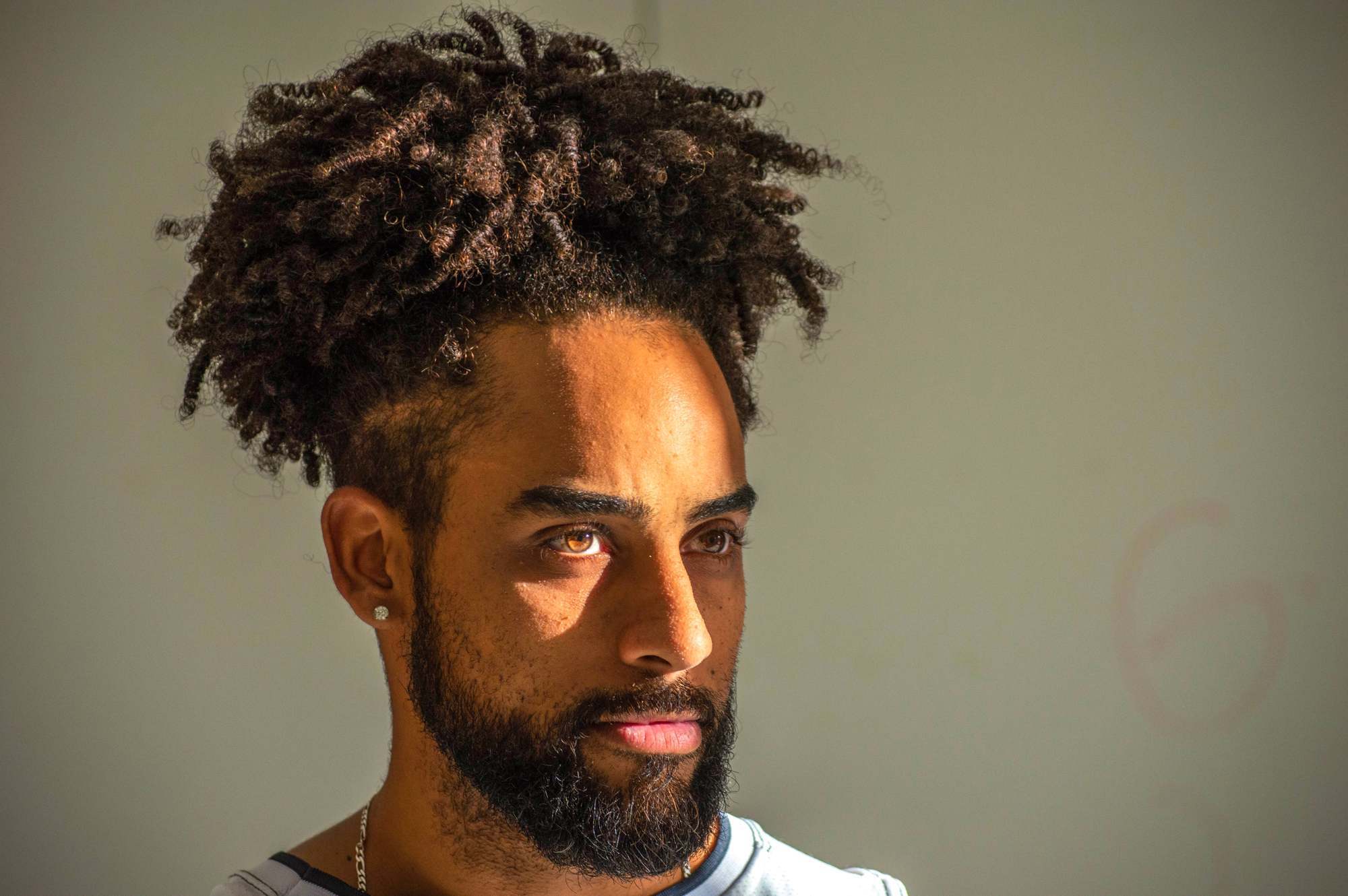 Homem de barba e cabelo degrade crespo com tranças e dreads no topo usa acessórios