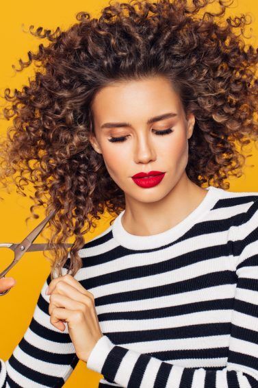 Mulher com cabelos cacheados corta o cabelo sozinha com tesoura