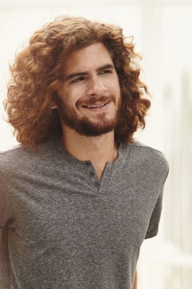 Homem de camiseta cinza, ao ar livre, mstra como definir cachos no cabelo masculino