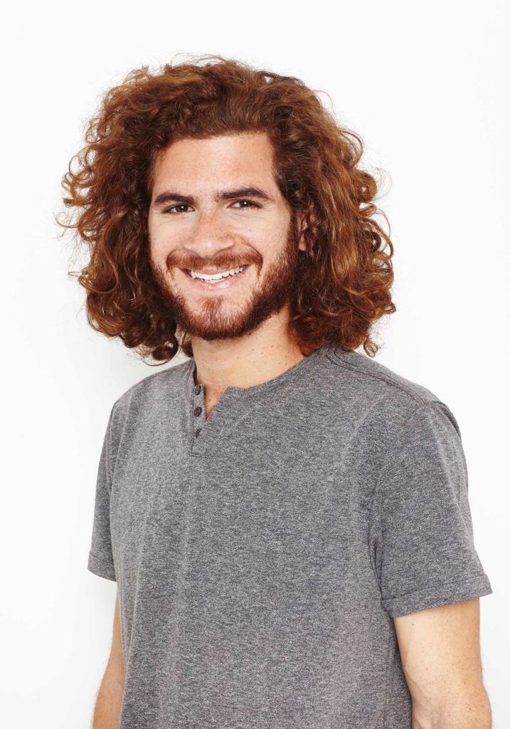Homem ruivo sorri, após mostrar como definir cachos no cabelo masculino