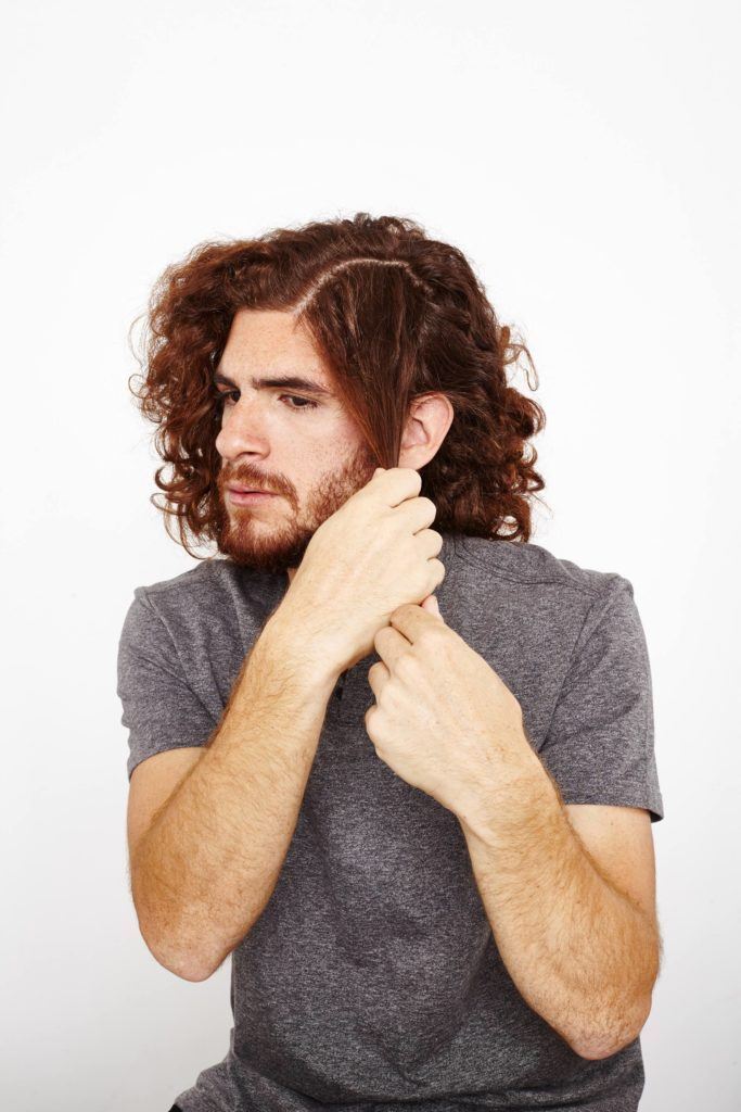 Homem passa produto nas mechas para definir cachos no cabelo masculino