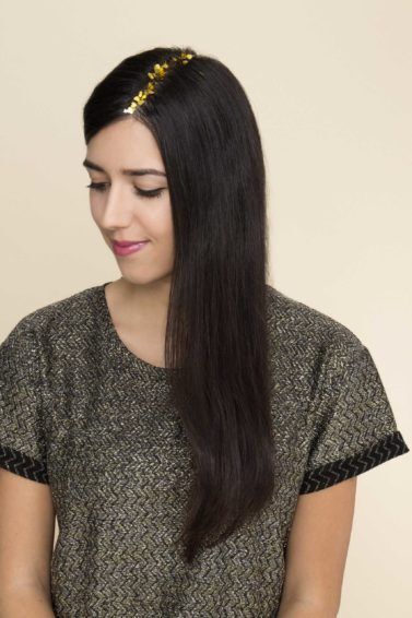 Mulher com cabelo comprido, liso e preto veste camiseta cinza e usa glitter dourado no cabelo