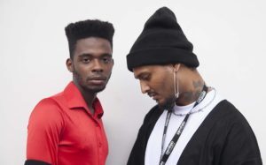 Dois homens posam e um deles usa high top fade