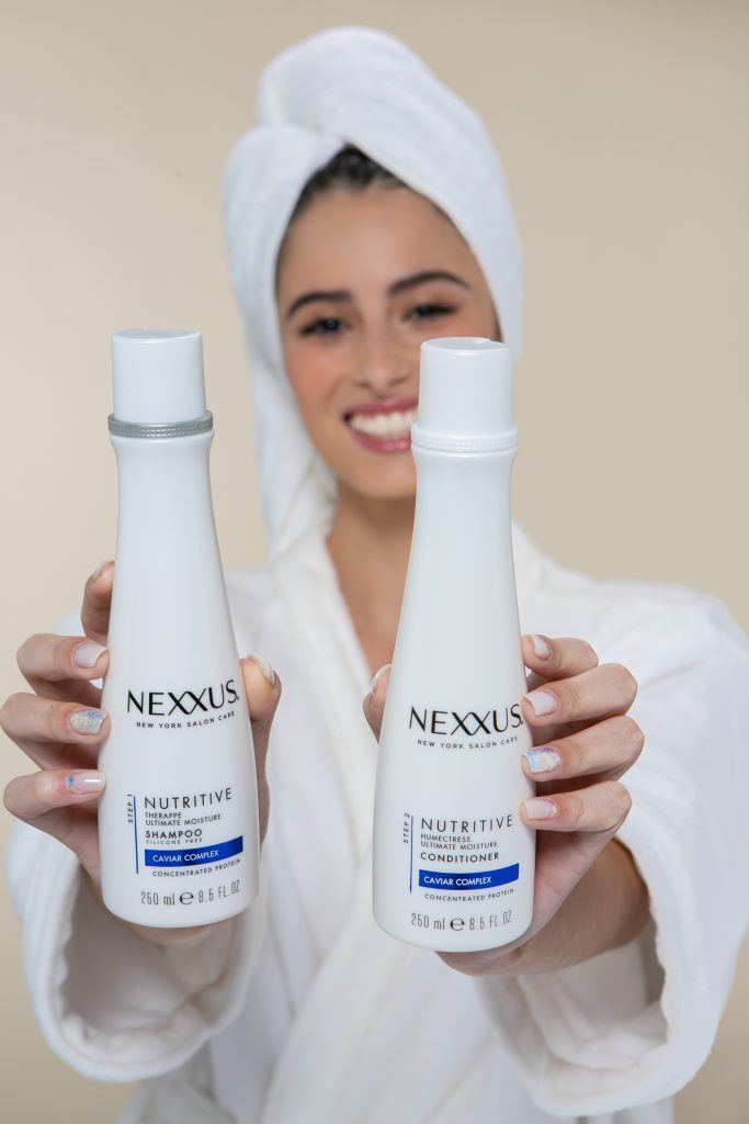 Mulher om toalha na cabeça segurando shampoo e condicionador