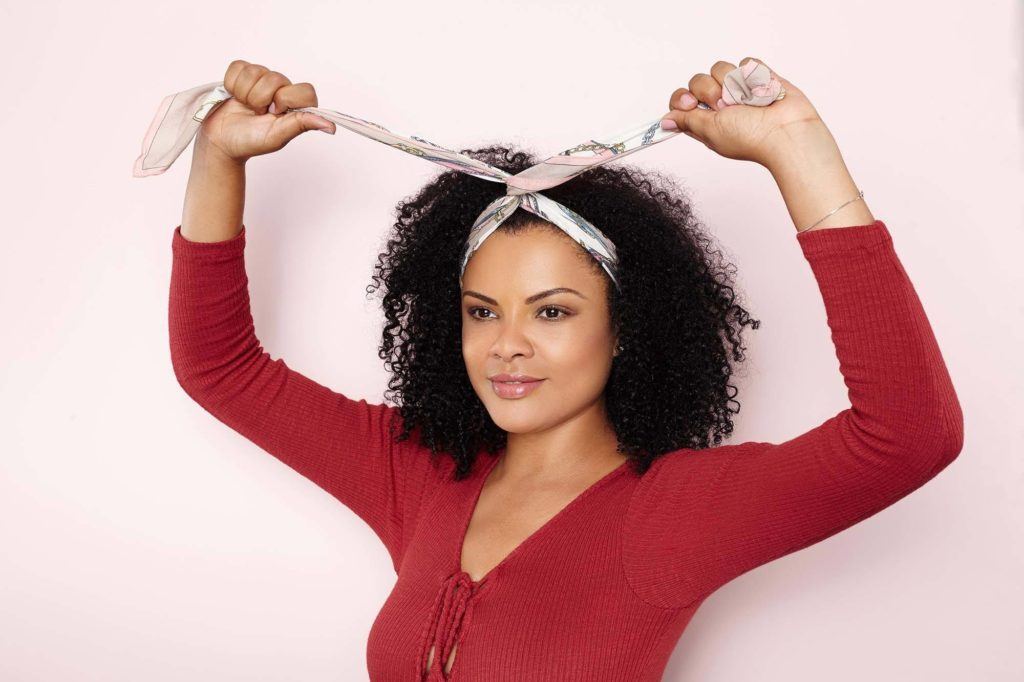 Mulher com cabelo afro amarrando um lenço na cabeça