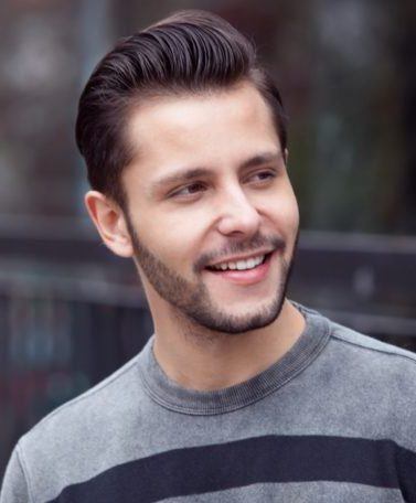 Homem usa camisa listrada cinza e preta e, no cabelo o quiff, um topete com charme discreto