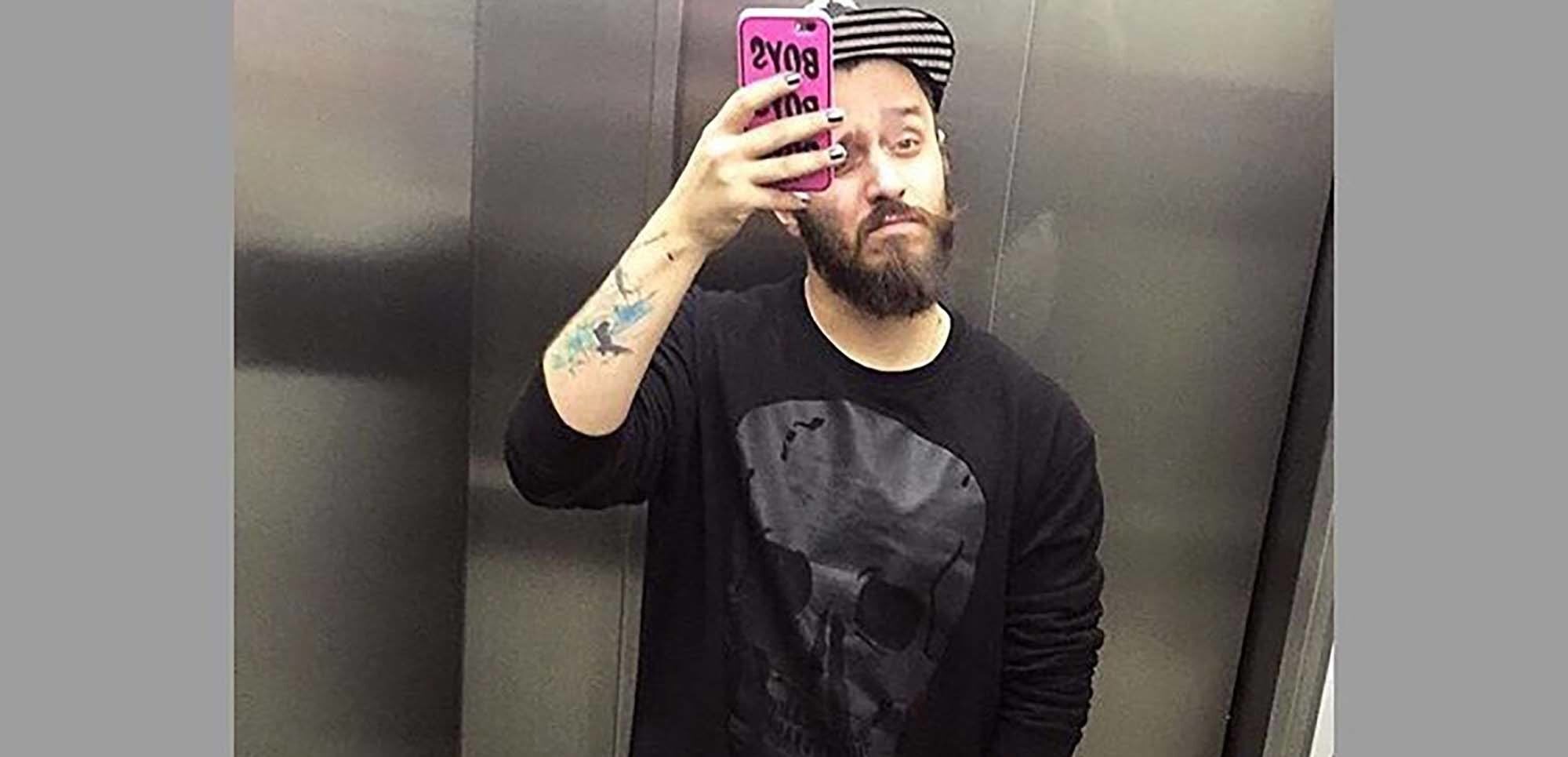 Homem tira selfie no elevador, vestindo roupa toda preta.