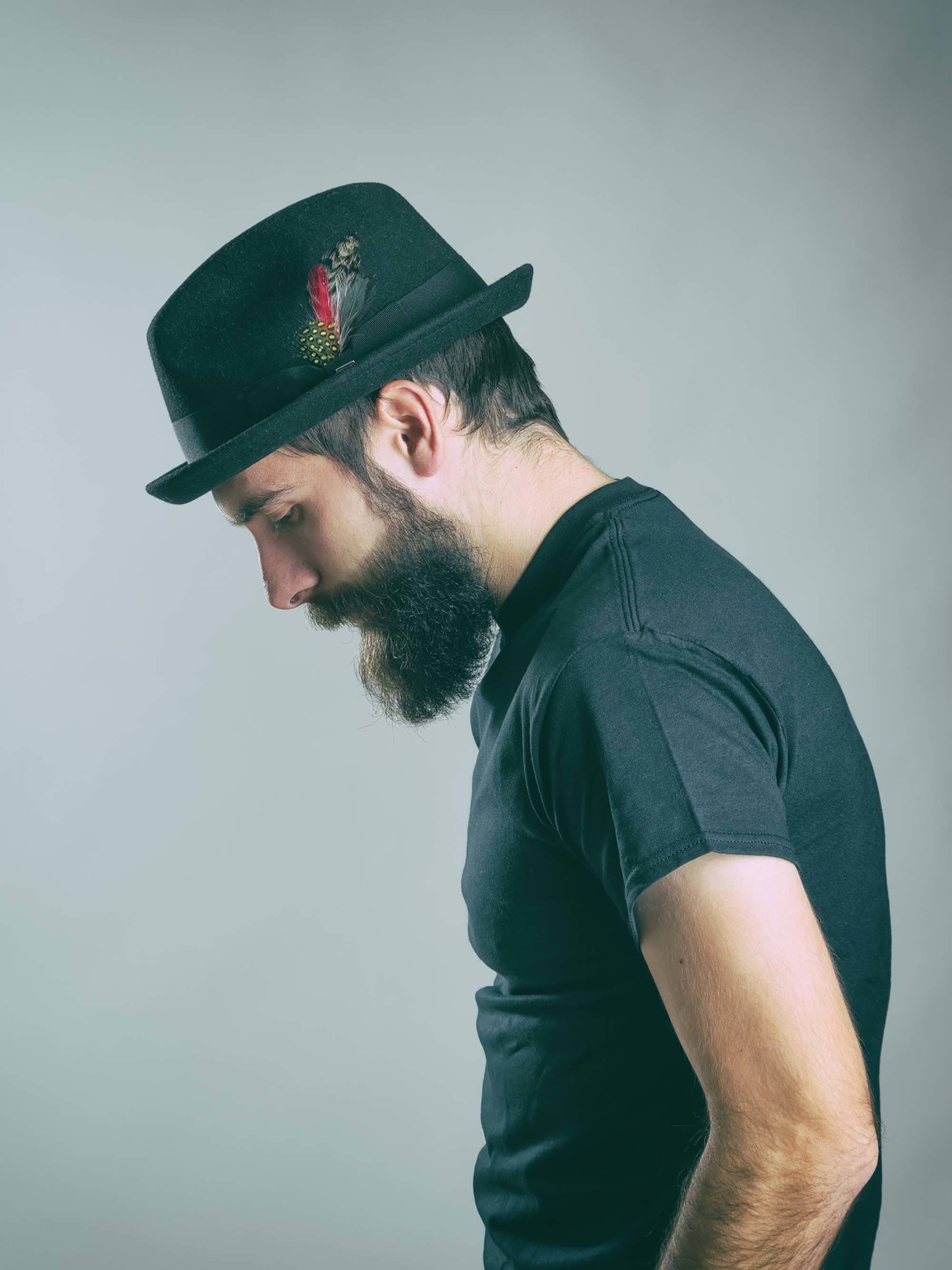 Homem usa chapéu e camiseta preta e ilustra matéria sobre penteados para homens no Carnaval