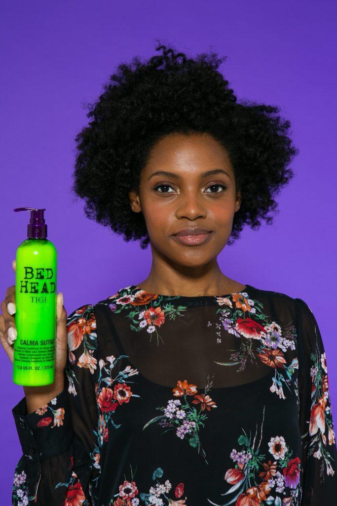 Modelo com produto na mão e blusa preta com detalhe de flores coloridas
