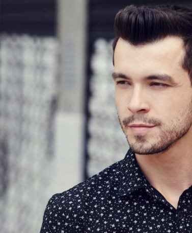 Homem usa camisa preta com estampa branca e, no cabelo, quiff texturizado