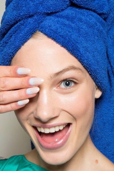 mulher com toalha de banho enrolada no cabelo tapa um dos olhos enquanto sorri
