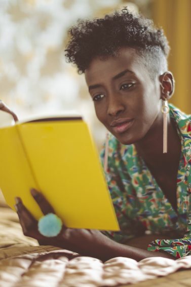 Mulher com cabelo crespo curto lê livro com capa amarela