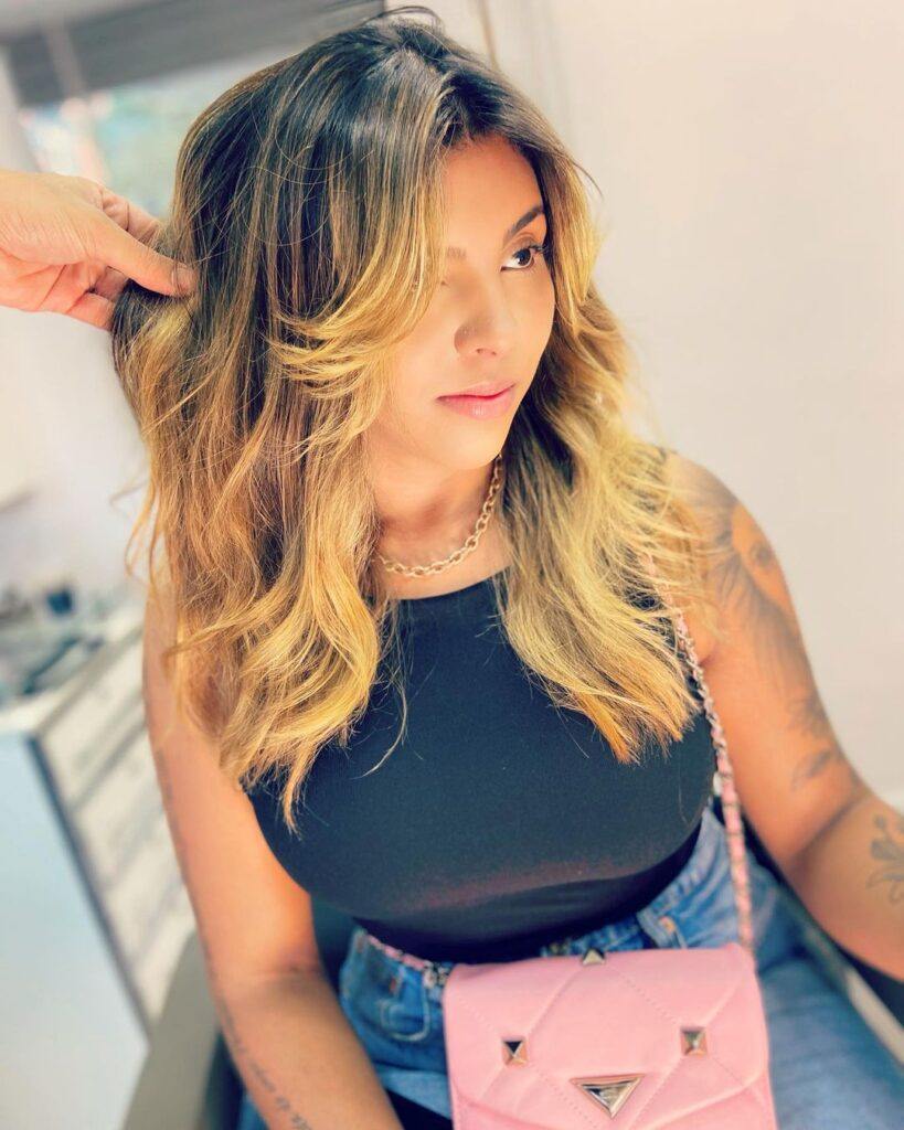 mulher mostra o cabelo em camadas morena iluminada com franja longa
