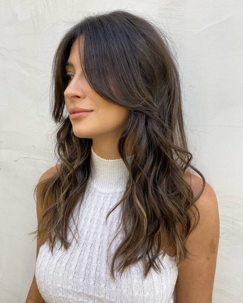 mulher de lado com blusa branca mostra cabelo comprido ondulado em camadas com franja longa