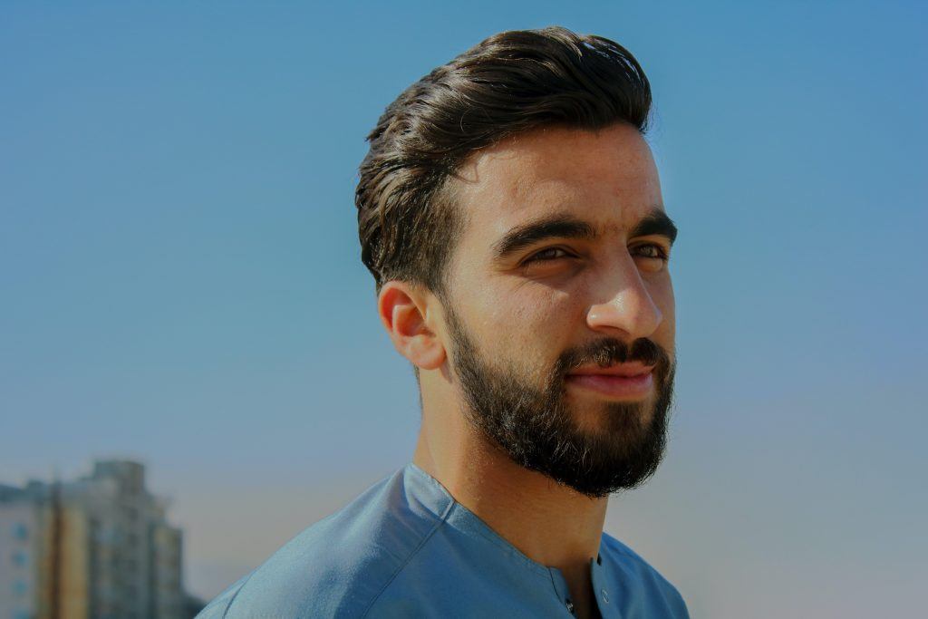 Homem de barba e cabelo pretos e camisa azul, ao ar livre