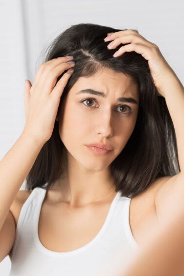 mulher segurando o cabelo olhando preocupada para o couro cabeludo