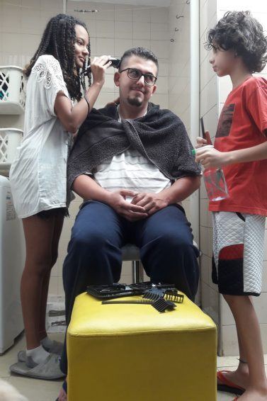 Filhos cortam o cabelo do pai: na foto, estão Vitória (à esq.) e Ian (à dir.), que cortam o cabelo de Anderson