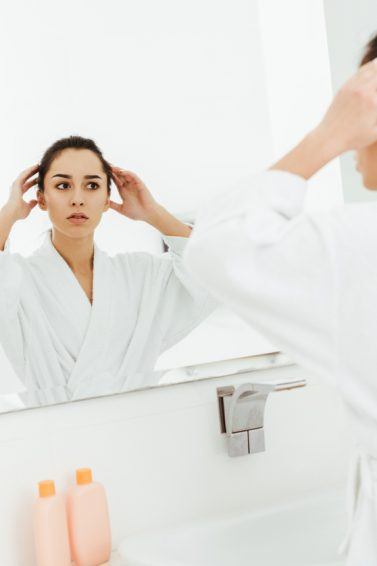 mulher com cabelo preso se olhando no espelho