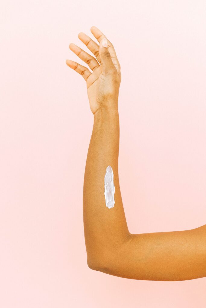 braço em fundo rosa com creme hidratante