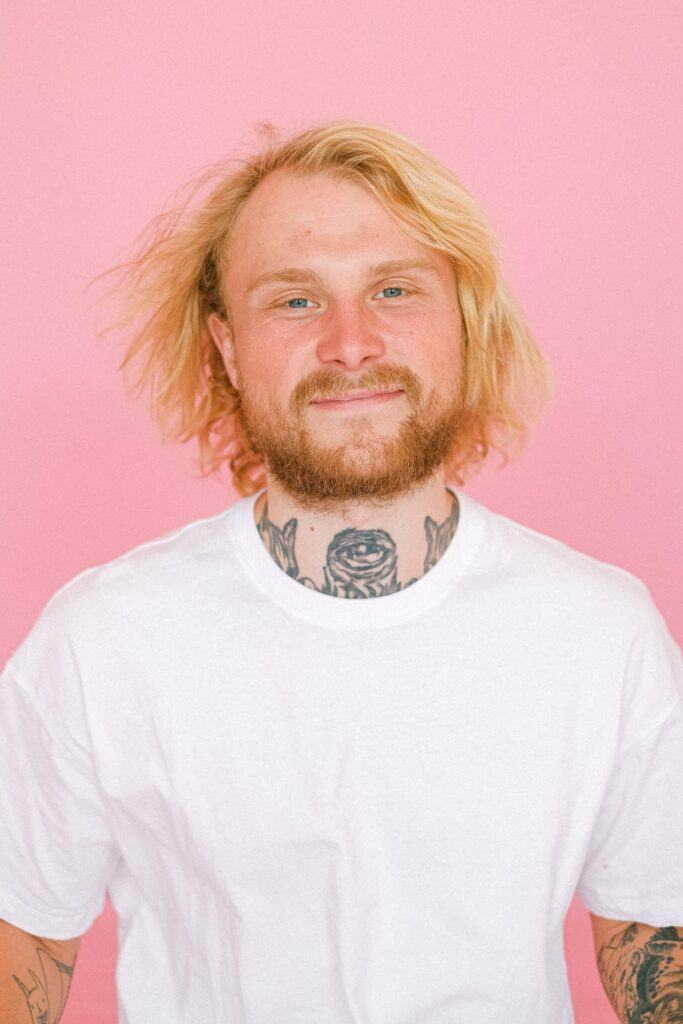 homem sorrindo com tatuagem, barba e cabelo loiro