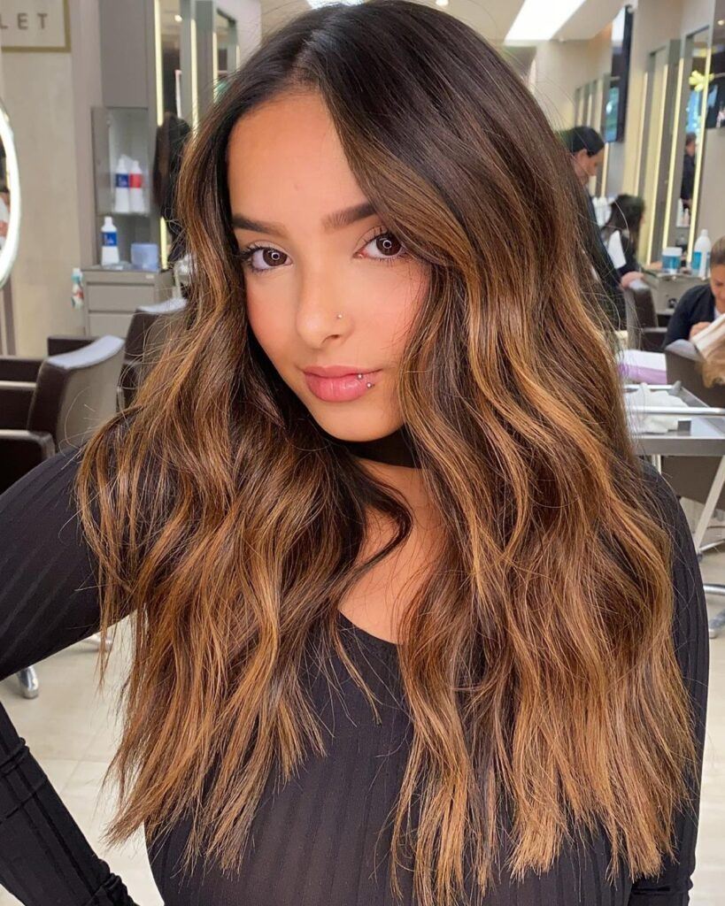 mulher com cabelos castanhos e mechas iluminadas no estilo ombre hair