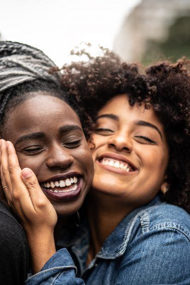 Duas amigas com cabelos cacheados e afro se abraçam