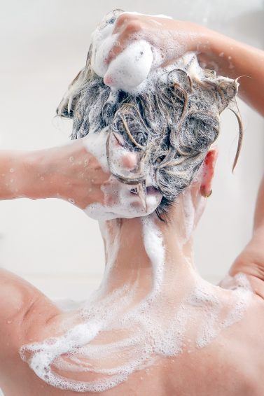 Mulher lava os cabelos no box e faz espuma com o shampoo
